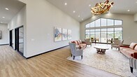 Located at 1600 Kityhawk Drive in Columbia, Missouri, this two-floor amenity building offers a generous and well-appointed space designed for both relaxation and active living. The main floor welcomes visitors through a glass-framed double-door entry that sets a modern, open tone. The combined living and dining area is a standout, showcasing soaring vaulted ceilings, warm light wood flooring, and a dramatic floor-to-ceiling window wall that frames sweeping views of the outdoor pool and surrounding neighborhood. A sculptural gold chandelier adds an elegant focal point, while curated abstract artwork and thoughtfully arranged seating lend the space a refined yet comfortable atmosphere. High bar-height tables near the expansive windows create an ideal spot for casual gatherings with scenic views. The second floor mirrors the building's generous square footage and provides additional lounge space, also benefiting from large windows and natural light. The dedicated fitness center is a highlight of the lower level, featuring polished concrete floors, an exposed industrial ceiling with structural steel and linear lighting, and an extensive array of equipment including treadmills, stationary bikes, rowing machines, ellipticals, free weights, and resistance tools. Glass doors in the fitness area open directly to the outdoors, ensuring excellent ventilation and natural light throughout the workout space.