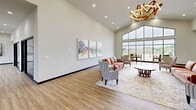 Located at 1600 Kityhawk Drive in Columbia, Missouri, this two-floor amenity building offers a generous and well-appointed space designed for both relaxation and active living. The main floor welcomes visitors through a glass-framed double-door entry that sets a modern, open tone. The combined living and dining area is a standout, showcasing soaring vaulted ceilings, warm light wood flooring, and a dramatic floor-to-ceiling window wall that frames sweeping views of the outdoor pool and surrounding neighborhood. A sculptural gold chandelier adds an elegant focal point, while curated abstract artwork and thoughtfully arranged seating lend the space a refined yet comfortable atmosphere. High bar-height tables near the expansive windows create an ideal spot for casual gatherings with scenic views. The second floor mirrors the building's generous square footage and provides additional lounge space, also benefiting from large windows and natural light. The dedicated fitness center is a highlight of the lower level, featuring polished concrete floors, an exposed industrial ceiling with structural steel and linear lighting, and an extensive array of equipment including treadmills, stationary bikes, rowing machines, ellipticals, free weights, and resistance tools. Glass doors in the fitness area open directly to the outdoors, ensuring excellent ventilation and natural light throughout the workout space.