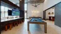 Located at 3000 Cypress Lake Rd in North Charleston, SC, this single-story amenity space showcases a sophisticated contemporary design defined by soaring ceilings and an abundance of natural light. The main lounge area features floor-to-ceiling windows that frame lush outdoor views, filling the space with daylight and creating an airy, open atmosphere. Large-format light tile flooring runs throughout, unifying the various zones seamlessly.

Distinctive reclaimed wood columns and ceiling beams provide a warm, textural contrast to the crisp white walls, lending the corridors and gathering areas a refined yet approachable character. Sculptural pendant lighting installations add artistic flair throughout.

The social hub includes a well-appointed game room featuring a pool table, shuffleboard, large-screen television, and bar-height seating—all beneath dramatic high ceilings. An adjacent kitchen area offers a sleek island with woven bar stools, stainless steel appliances, and wall-mounted media for casual entertaining.

Quieter nooks provide intimate seating with stylish furnishings and curated wall art, offering more private settings within the broader communal environment. Wide, gallery-style corridors display artwork and connect each functional zone, contributing to the space's polished, resort-inspired ambiance throughout.