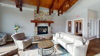 Located on Abbey Court in Onalaska, Wisconsin, this single-story community clubhouse offers a comprehensive range of amenities designed for comfort and recreation. The main lounge area is a standout, featuring soaring wood-beamed ceilings with rich timber accents, a dramatic floor-to-ceiling stacked stone fireplace with a wood mantel, and comfortable seating arranged for relaxed gatherings. Adjacent to the lounge, a bright dining area benefits from the same striking vaulted wood ceiling and large windows that frame scenic outdoor views, with direct access to an outdoor patio. The full kitchen is well-equipped with granite countertops, a large center island with bar seating, stainless steel appliances, custom cabinetry, and a tile backsplash. A dedicated game room features a full-size billiards table beneath an elegant coffered ceiling with large interior windows. The spacious fitness center is fully outfitted with strength training equipment, cardio machines, free weights, and a variety of functional training accessories, all reflected by floor-to-ceiling mirrors. A private whirlpool room with wood-toned tile finishes and natural light provides a relaxing retreat. Marble-tiled corridors, a water station, and restroom facilities complete this thoughtfully designed community space.