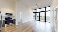 Located in Miami's vibrant Coral Way neighborhood, this single-floor unit showcases a clean, contemporary design throughout. The open living area immediately impresses with its notably tall ceilings and crisp white walls, creating a bright, airy atmosphere. Light wood-tone flooring runs continuously throughout, lending warmth and visual cohesion to the space.

Floor-to-ceiling glass sliding doors frame striking city views and lead directly to a private outdoor balcony, flooding the interior with abundant natural light. The living area flows seamlessly into the kitchen, which is outfitted with stainless steel appliances — including a full-size refrigerator with ice maker, electric range, built-in microwave, and dishwasher. Two-toned cabinetry featuring charcoal lower cabinets and crisp white upper cabinets pairs with light countertops for a modern aesthetic.

A separate bedroom also benefits from floor-to-ceiling glass doors opening to an outdoor area, continuing the unit's emphasis on natural light and outdoor connectivity. The bathroom features distinctive wood-grain tile surround in the tub/shower combination, complemented by large-format floor tiles, a sleek vanity with a light countertop, and gray cabinetry — delivering a refined, spa-inspired finish.