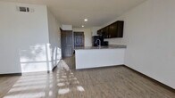 This single-floor unit offers a thoughtfully designed open-concept layout that seamlessly connects the kitchen and living area. The kitchen is a standout feature, anchored by a large granite-topped peninsula with an integrated sink, providing generous counter space and a natural gathering point. Dark espresso cabinetry lines the walls above, complemented by black appliances including a refrigerator, range, and over-the-range microwave. Light wood-look flooring runs consistently throughout the space, lending a clean and cohesive aesthetic.

The living area is bright and open, benefiting from natural light that streams in through slatted window blinds, casting distinctive light patterns across the floor. The entry foyer is defined by a solid six-panel front door, with additional interior doors providing access to adjoining rooms.

The bedrooms are well-proportioned, each featuring the same wood-look flooring, neutral white walls, and windows that allow for natural light. The rooms offer versatile, flexible layouts suitable for a variety of uses.

The bathroom is outfitted with a tub-shower combination featuring floor-to-ceiling gray tile surround, a granite-topped vanity with dark cabinetry, and brushed nickel fixtures, delivering a consistent and polished finish that ties the unit together.
