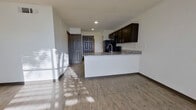This single-floor unit offers a thoughtfully designed open-concept layout that seamlessly connects the kitchen and living area. The kitchen is a standout feature, anchored by a large granite-topped peninsula with an integrated sink, providing generous counter space and a natural gathering point. Dark espresso cabinetry lines the walls above, complemented by black appliances including a refrigerator, range, and over-the-range microwave. Light wood-look flooring runs consistently throughout the space, lending a clean and cohesive aesthetic.

The living area is bright and open, benefiting from natural light that streams in through slatted window blinds, casting distinctive light patterns across the floor. The entry foyer is defined by a solid six-panel front door, with additional interior doors providing access to adjoining rooms.

The bedrooms are well-proportioned, each featuring the same wood-look flooring, neutral white walls, and windows that allow for natural light. The rooms offer versatile, flexible layouts suitable for a variety of uses.

The bathroom is outfitted with a tub-shower combination featuring floor-to-ceiling gray tile surround, a granite-topped vanity with dark cabinetry, and brushed nickel fixtures, delivering a consistent and polished finish that ties the unit together.