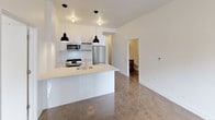 Located in the heart of Chicago's Loop at 2 E Adams Street, this single-floor unit offers a thoughtfully designed layout with a clean, contemporary aesthetic throughout. Polished concrete floors extend across the entire space, lending an industrial-modern character that ties each area together seamlessly.

The open-concept kitchen is a standout feature, anchored by a white waterfall island with an undermount sink and stylish black pendant lighting overhead. White cabinetry lines the walls, complemented by a full suite of stainless steel appliances including a gas range, microwave, and refrigerator — providing both function and visual appeal.

The living area flows naturally from the kitchen, offering an open and airy feel with crisp white walls and generous ceiling height. A dedicated bedroom features a wall-mounted split HVAC unit for personalized climate control, a large window framing views of the surrounding Chicago skyline, and access to a spacious closet with built-in shelving for ample storage.

The bathroom is finished with a dark wood-tone vanity with open shelving, a white countertop, a gold-accented faucet, and a mirrored medicine cabinet — combining practicality with refined detail. The overall palette of white walls, polished floors, and modern fixtures creates a cohesive, minimalist atmosphere well-suited to urban living in one of Chicago's most iconic downtown neighborhoods.