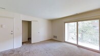 This single-floor residence offers a clean, functional layout designed for comfortable everyday living. The main living area is generously proportioned, featuring neutral wall-to-wall carpeting that adds warmth underfoot and a soft, understated aesthetic throughout. Crisp white ceilings and light-toned walls create a bright, open atmosphere that feels welcoming and versatile.

A standout feature of the main room is the large sliding glass door that opens to a private balcony enclosed by a classic brick railing. This door floods the interior with natural light and provides pleasant views of the surrounding greenery, creating a seamless connection between the indoor and outdoor spaces.

The room also includes a floor-mounted HVAC vent, ensuring efficient climate control year-round. A sliding door along one wall leads to an adjacent room or closet space, adding to the overall functionality and storage potential of the layout.

The space is presented in a neutral, move-in ready condition, offering a blank canvas that can easily be personalized to suit a variety of tastes and furnishing styles. The combination of natural light, outdoor access, and a straightforward, practical floor plan makes this a well-rounded residential space suitable for a range of living arrangements.