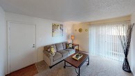 This single-story residence offers a thoughtfully laid-out floor plan designed for comfortable everyday living. The living area is warm and inviting, featuring carpet flooring, a textured ceiling, and a sliding glass door fitted with vertical blinds that allows natural light to filter in. The space flows seamlessly into a dedicated dining area, which is equipped with a ceiling fan and a window, creating a bright and functional space for meals and gathering.

The galley-style kitchen is efficiently designed with ample white cabinetry, a stainless steel sink, hardwood-style flooring, and a full suite of white appliances including a refrigerator, electric range, and dishwasher. A small window brings in additional natural light, enhancing the kitchen's clean and practical atmosphere.

The two bedrooms are comfortably sized, each featuring plush carpet flooring, ceiling fans with light fixtures, and windows dressed with curtains that offer both privacy and natural light. The rooms provide a restful retreat with neutral wall tones that lend a calm ambiance.

The bathroom is well-appointed with a single-sink vanity topped by a large mirror and vanity lighting, a toilet, and a full tub-shower combination. Hardwood-style flooring and a textured ceiling complete the space. Overall, this residence combines practical design with comfortable living spaces suited for daily life.