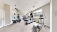 Located at 1724 Robb St in Lakewood, Colorado, this 24-hour fitness center offers a thoughtfully organized workout space designed to accommodate a full range of exercise routines. The single-floor gym is finished with neutral, light-toned walls and low-pile patterned carpeting that gives the space a clean, professional appearance. Vaulted ceilings in portions of the room add a sense of openness, while multiple large windows along the perimeter flood the interior with natural light and provide views of the surrounding greenery outdoors.

The cardio zone is well-stocked with a lineup of Spirit treadmills, elliptical trainers, and a stationary bike, all arranged to take advantage of the natural light from the windows. A wall-mounted flat-screen television is positioned for easy viewing during cardio sessions. The strength training area features multi-function cable and weight machines, along with a dedicated free weights section equipped with a dumbbell rack and an adjustable workout bench. A large mirror panel is mounted along one wall to support proper form during exercise.

The facility includes a direct exterior entrance with a coat hook area, posted gym rules, and an emergency exit, ensuring convenience and safety for all users. The overall ambiance is bright, functional, and inviting — well-suited for daily fitness use.