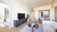 Located at 3401 S La Cienega Blvd in Los Angeles, this thoughtfully designed two-bedroom, one-bathroom residence offers a seamless blend of modern aesthetics and functional living. The open living room is anchored by light hardwood flooring and floor-to-ceiling sliding glass doors that lead to a private balcony, flooding the space with natural light and offering expansive views of the Los Angeles skyline. The kitchen features a professional-grade stainless steel range with an induction cooktop, sleek light-blue cabinetry with under-cabinet lighting, and light stone countertops. The primary bedroom is generously proportioned, featuring large windows with city views and warm, neutral tones. The second bedroom offers a cozy, well-appointed retreat with soft carpet and stylish decor. A dedicated walk-in closet with dual hanging rods and hardwood flooring provides ample storage. The bathroom is finished with a checkered tile floor, a wood-fronted vanity, an undermount sink, and a backlit mirror. A connecting hallway ties all rooms together efficiently, completing this well-appointed urban residence.