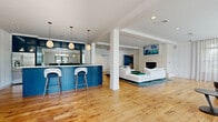 Located at 597 Westport Ave in Norwalk, CT, this thoughtfully designed single-floor amenity space offers a generous, open-concept layout that seamlessly connects multiple functional areas. Warm hardwood flooring runs throughout, unifying the space and complementing the clean, modern aesthetic defined by white paneled walls and recessed lighting.

The kitchen is a standout feature, showcasing bold navy-blue cabinetry with glass-front upper cabinets, stainless steel appliances including a side-by-side refrigerator and beverage cooler, a white quartz waterfall island with bar seating, and elegant pendant lighting overhead. It opens directly into the main lounge area, which centers around a stone-surround fireplace flanked by a plush white sectional sofa. Curated artwork adds a vibrant, creative touch to the walls.

The lounge extends into a bright seating area lined with floor-to-ceiling sheer-draped windows that flood the room with natural light and offer views of the surrounding greenery. Curved gray lounge chairs and high-top bistro tables provide flexible seating arrangements suited for both casual and social settings.

The game room is a lively retreat featuring a regulation pool table beneath a dramatic tiered pendant light, a glossy navy ceiling, a large wall-mounted TV, foosball table, and arcade games — all centered on a richly patterned area rug.