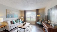 Located at 2870 Kengary Way in Reynoldsburg, Ohio, this single-floor residence offers a well-designed layout with a cohesive, contemporary aesthetic throughout. The living room serves as the heart of the home, featuring wood-look flooring, a large window with views of the outdoors, and a textured ceiling that adds visual interest. A dedicated sitting nook with teal accent chairs and a console table provides a secondary gathering space within the living area. The kitchen is thoughtfully appointed with white cabinetry, light countertops, a peninsula for casual dining, and black appliances including a refrigerator, range, and dishwasher, all set on durable wood-look flooring. The primary bedroom is generously proportioned with plush carpet, natural light from a large window, and a walk-in closet offering ample storage. A versatile flex room, also carpeted, functions as an office or secondary lounge. The bathroom features wood-look flooring, a tub-shower combination, a vanity with storage, and a built-in open shelving unit. A secondary bathroom provides additional convenience. Neutral tones with teal and warm wood accents create a welcoming, modern ambiance throughout the entire space.