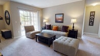 The Colchester's 2-bedroom, 2-bathroom floor plan is thoughtfully arranged on a single level, providing a functional and comfortable living environment. The living room serves as the heart of the home, featuring neutral-toned carpet, warm beige walls, and a large sliding glass door that invites abundant natural light and provides outdoor views. The open layout connects seamlessly to the rest of the residence.

The galley-style kitchen is equipped with honey-toned oak cabinetry, white appliances including a range, refrigerator, and dishwasher, and durable wood-look flooring. Adjacent to the kitchen, the dining area features the same flooring, a ceiling fan with light fixture, and a closet for added storage.

The primary bedroom is generously sized with carpet flooring, multiple windows offering natural light, and access to a spacious walk-in closet with built-in shelving. Its en-suite bathroom includes a tub-shower combination. The second bedroom also features carpet and a window, serviced by a second full bathroom with a tub-shower, wood-toned vanity, and tile flooring. Throughout, neutral tones and consistent finishes create a cohesive and welcoming ambiance.