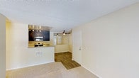 Located at 4302 Calle Odessa in Carlsbad, this single-floor residence offers a practical and comfortable open-concept layout. The kitchen is a standout feature, equipped with dark navy cabinetry, granite-style countertops, stainless steel appliances including a microwave and range, and track lighting overhead that highlights the space. The kitchen flows seamlessly into the adjoining living and dining areas, creating an inviting and connected environment.

The living area is finished with plush wall-to-wall carpeting, while the transitional space leading toward the entry and beyond features durable hardwood-style flooring, providing both comfort and practicality. A ceiling fan is centrally positioned to promote air circulation throughout the open living space. The walls are painted in a neutral, warm tone that enhances the sense of brightness and openness.

A textured ceiling adds a classic touch throughout the interior. The entry door and interior doors are finished in clean white, contributing to a cohesive and tidy aesthetic. Ample wall space and a straightforward layout make this residence highly functional, offering a welcoming atmosphere well-suited to everyday living in the desirable Carlsbad community.
