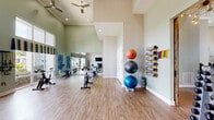 Located at 356 Lake Murray Boulevard in Columbia, SC, this fitness center offers a comprehensive and thoughtfully organized workout facility across a single, generously sized floor. The space is divided into distinct functional zones, each designed to support a variety of exercise routines and fitness goals.

The strength training area features an impressive array of selectorized weight machines, a full dumbbell rack, and benches, all set on durable, cushioned carpet flooring. Large windows along the walls flood the room with natural light and provide views of the surrounding neighborhood, while ceiling fans overhead maintain comfortable airflow. Crown molding and soaring ceilings lend the space a refined, upscale ambiance.

The cardio and functional training zone showcases smooth wood-look flooring, spin bikes, and a wide assortment of accessories including stability balls, yoga mats, resistance bands, kettlebells, and step platforms. Wall-mounted mirrors expand the sense of space, and wall-mounted flat-screen televisions are positioned for convenient viewing during workouts.

A rustic barn-style sliding door adds a charming architectural detail, connecting areas of the facility with character. The overall design balances functionality with an inviting atmosphere, making this fitness center a well-rounded destination for residents seeking a complete exercise experience.
