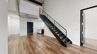 Located at 1700 Western Ave in Albany, NY, this two-story space offers a thoughtfully designed modern interior with industrial loft-inspired character. The expansive main floor features an open-concept kitchen and living area bathed in natural light, with wide-plank hardwood flooring throughout. The kitchen is appointed with dark cabinetry, a large white waterfall island with an integrated sink, and a full suite of stainless steel appliances including a refrigerator, range, and microwave. A striking open-tread black steel staircase serves as a bold architectural centerpiece, connecting the main floor to the upper level. Exposed spiral ductwork adds an industrial aesthetic that runs through multiple rooms. The upper floor houses the bedrooms, each featuring plush carpet flooring and soaring angled ceilings that amplify the sense of volume. The primary bedroom benefits from direct access to a well-appointed bathroom. Both bathrooms feature dark vanities with white countertops, vessel sinks, and clean-lined walk-in showers with hardwood-style flooring. A dedicated laundry room on the upper level includes a full-size washer and dryer. Two closets provide ample storage throughout the space.