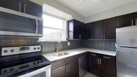 Located at 10900 Bustleton Avenue in the Northeast Philadelphia neighborhood of Philadelphia, PA, this single-floor space offers a clean, modern aesthetic throughout. The kitchen stands as a highlight of the unit, showcasing dark espresso-toned cabinetry that extends from floor to ceiling, providing generous storage. Crisp white countertops offer a striking contrast against the rich cabinet tones, while a sleek gray tile backsplash adds texture and depth to the space. The kitchen is equipped with stainless steel appliances, including an over-the-range microwave and an electric range, complemented by a stainless steel undermount sink with a contemporary arc-neck faucet. A bright window above the sink allows natural light to pour in, creating an inviting and functional cooking environment. The layout is designed for efficiency, with an L-shaped configuration that maximizes counter space and workflow. The overall design of the space reflects a contemporary sensibility, with cohesive finishes and attention to detail that make it a practical and visually appealing environment. The single-floor layout ensures easy accessibility and a seamless flow throughout the space.