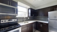 Located at 10900 Bustleton Avenue in the Northeast Philadelphia neighborhood of Philadelphia, PA, this single-floor space offers a clean, modern aesthetic throughout. The kitchen stands as a highlight of the unit, showcasing dark espresso-toned cabinetry that extends from floor to ceiling, providing generous storage. Crisp white countertops offer a striking contrast against the rich cabinet tones, while a sleek gray tile backsplash adds texture and depth to the space. The kitchen is equipped with stainless steel appliances, including an over-the-range microwave and an electric range, complemented by a stainless steel undermount sink with a contemporary arc-neck faucet. A bright window above the sink allows natural light to pour in, creating an inviting and functional cooking environment. The layout is designed for efficiency, with an L-shaped configuration that maximizes counter space and workflow. The overall design of the space reflects a contemporary sensibility, with cohesive finishes and attention to detail that make it a practical and visually appealing environment. The single-floor layout ensures easy accessibility and a seamless flow throughout the space.