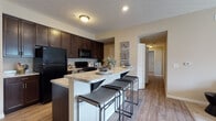 Located at 7220 E Broad St in Columbus, Ohio, this single-floor residence offers a thoughtfully designed layout that balances functionality with comfort. The open-concept kitchen is a central highlight, showcasing rich dark espresso cabinetry, granite-style countertops, a tile backsplash, and black appliances including a refrigerator, range, and built-in microwave. A spacious breakfast bar with bar seating provides an ideal spot for casual dining, while a dedicated pantry with open shelving offers generous storage. Wood-style flooring flows throughout the main living areas, adding warmth and continuity. The living room is bright and inviting, featuring plush carpeting and French doors that open to a private balcony with outdoor views. Multiple bedrooms are carpeted for comfort, each with windows that bring in natural light and ample space for furnishings. The bathrooms are finished with tile flooring, dark vanity cabinetry with marble-style countertops, and a tub-shower combination. Neutral wall tones throughout the residence create a versatile backdrop that complements a variety of interior styles. The overall ambiance is warm, practical, and move-in ready, offering a comfortable living experience in a convenient Columbus location.