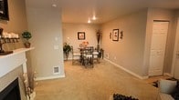 This single-floor space features a well-appointed dining area set against a backdrop of warm, neutral-toned walls that contribute to a calm and welcoming ambiance. The dining space is centered around a round table accompanied by four metal-framed chairs with upholstered seats, offering a practical yet stylish setting for meals and gatherings. Recessed ceiling lights provide even, focused illumination throughout the room, enhancing the cozy atmosphere. Soft, wall-to-wall carpeting in a beige tone adds warmth underfoot and complements the overall color palette. Decorative touches include framed botanical artwork on the walls, a tall dried floral arrangement, and a potted plant that introduces a natural element to the space. A small accent table tucked against the wall provides additional surface space. Baseboards and a floor-level vent are visible, reflecting functional infrastructure integrated neatly into the design. A partial wall or column near the entry adds architectural dimension, subtly defining the dining area from adjacent spaces. Overall, the space presents a tidy, comfortable environment well-suited for everyday living.
