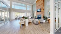 Located at 9345 Blue House Rd in North Charleston, SC, this single-floor space makes a striking architectural impression from the moment you enter. The living area is defined by dramatic double-height ceilings that amplify the sense of openness, complemented by expansive floor-to-ceiling windows and glass walls that flood the interior with natural light and offer views of the surrounding outdoors.

The living room serves as the centerpiece of the space, anchored by a bold, full-height natural wood accent wall housing a sleek fireplace — a standout design element that draws the eye upward and adds warmth to the contemporary aesthetic. Light hardwood flooring runs throughout, lending a clean, cohesive look that ties the various zones together seamlessly.

A glass-enclosed office or meeting area is integrated into the layout, providing a visually connected yet distinct functional space. Elegant décor details — including gold sculptural mirrors, curated greenery, and designer lighting fixtures — contribute to the refined, modern ambiance. A lounge area with plush neutral seating and a separate dining nook with a round table complete the thoughtfully arranged floor plan. The overall atmosphere is bright, airy, and polished, balancing sophisticated design with a welcoming, comfortable feel.