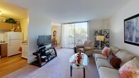 Located at 1145 Village Grove Dr in Elk Grove Village, IL, this single-floor residence offers a well-organized layout designed for comfortable everyday living. The living room is a welcoming space finished with plush carpeting and neutral walls, anchored by a large floor-to-ceiling window dressed with vertical blinds that bathe the room in natural light and offer pleasant outdoor views. The open feel is complemented by a glass-top coffee table and ample seating area.

Adjacent to the living room, the dining area accommodates a full-sized wooden dining table and benefits from its own window, allowing additional natural light to filter in. A decorative mirror adds depth to the space.

The kitchen features warm oak cabinetry extending to the ceiling for generous storage, light-colored countertops, a gas range, refrigerator, and hardwood-style flooring. The efficient galley-style layout keeps everything within easy reach.

The bedroom is generously sized with soft carpeting, a ceiling fan with light fixture, and multiple windows that invite natural light. Baseboard heating runs along the perimeter, ensuring year-round comfort.

The bathroom includes a tub-shower combination with a bold striped curtain, a wood-toned vanity, a large wall mirror with Hollywood-style lighting, and classic tile flooring throughout.