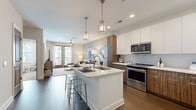 Located at 2001 Commerce St in Alpharetta, GA, this well-appointed one-bedroom, one-bathroom residence offers a thoughtfully designed open-concept layout. The kitchen is a standout feature, showcasing a two-toned design with glossy white upper cabinets and warm walnut-finish lower cabinets, a light subway tile backsplash, quartz countertops, and a full suite of stainless steel appliances. A central island with seating for two and pendant lighting above creates a natural gathering point that flows seamlessly into the living area. The living room is bright and welcoming, featuring dark hardwood-style flooring, neutral tones, and French doors that open to a private balcony overlooking the community courtyard. The bedroom is a comfortable retreat with plush carpeting, a ceiling fan, and large windows that invite abundant natural light and exterior views. The bathroom is sleekly finished with walnut cabinetry, a dual-sink vanity with a white quartz countertop, a large mirror with Hollywood-style lighting, and a glass-enclosed walk-in shower with built-in shelving. A dedicated closet provides additional storage. The overall ambiance is modern and clean, with consistent use of warm wood tones, crisp whites, and soft neutral walls throughout.