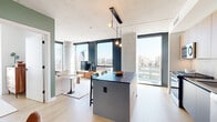 Located at 234 W Polk St in Chicago's vibrant West Loop neighborhood, this modern high-rise unit offers a thoughtfully designed open-concept layout with contemporary finishes throughout. Light oak hardwood flooring flows seamlessly from the entry hallway—accented with curated wall art—into the main living areas, establishing a warm, cohesive aesthetic.

The kitchen is a standout feature, equipped with stainless steel appliances, light wood cabinetry, and a dark-topped central island with bar seating beneath a sleek linear pendant light fixture. Floor-to-ceiling windows flood the space with abundant natural light and frame striking panoramic views of the Chicago skyline.

The open living and dining area is defined by sage green accent walls, a comfortable seating arrangement, and a round walnut dining table with sculptural leather chairs. Large-format artwork reinforces the curated, design-forward character of the space.

The bedroom offers city views through expansive dark-framed windows and includes a dedicated seating area, making it a versatile and restful retreat. The bathroom is finished with dark large-format tile, a soaking tub with overhead shower, and a wood-panel vanity with a white stone countertop. Exposed concrete ceiling details throughout add an industrial-modern contrast to the warm furnishings and soft color palette.