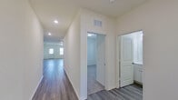 This single-story home offers a clean, modern aesthetic defined by a crisp white color palette, durable hardwood-style flooring, and plush carpet in the bedroom areas. The open-concept layout connects the kitchen and living area seamlessly, creating a generous and functional shared space bathed in recessed lighting.

The kitchen serves as a central feature, showcasing granite countertops with subtle veining, white shaker-style cabinetry, and a full suite of stainless steel appliances including a range, over-the-range microwave, and refrigerator. A central island provides additional prep space and casual seating potential.

A long, well-lit hallway connects the main living area to the private rooms, with ceiling vents ensuring consistent climate control throughout. The primary bedroom is carpeted and features windows that allow natural light to fill the space. Its en-suite bathroom includes a wide white vanity with ample drawer storage, a large mirror, and stylish light fixtures overhead. A walk-in closet with wire shelving and a full rod system provides organized storage.

Overall, the home presents a fresh, move-in-ready interior with consistent finishes and a practical, flowing layout.