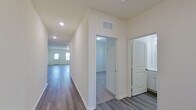 This single-story home offers a clean, modern aesthetic defined by a crisp white color palette, durable hardwood-style flooring, and plush carpet in the bedroom areas. The open-concept layout connects the kitchen and living area seamlessly, creating a generous and functional shared space bathed in recessed lighting.

The kitchen serves as a central feature, showcasing granite countertops with subtle veining, white shaker-style cabinetry, and a full suite of stainless steel appliances including a range, over-the-range microwave, and refrigerator. A central island provides additional prep space and casual seating potential.

A long, well-lit hallway connects the main living area to the private rooms, with ceiling vents ensuring consistent climate control throughout. The primary bedroom is carpeted and features windows that allow natural light to fill the space. Its en-suite bathroom includes a wide white vanity with ample drawer storage, a large mirror, and stylish light fixtures overhead. A walk-in closet with wire shelving and a full rod system provides organized storage.

Overall, the home presents a fresh, move-in-ready interior with consistent finishes and a practical, flowing layout.