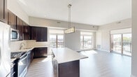 Located at 31 East Ogden Avenue in La Grange, IL, this well-appointed 3-bedroom, 2-bathroom residence offers a thoughtfully designed single-floor layout with a bright, modern aesthetic throughout. The open-concept kitchen and living area serves as the heart of the home, featuring rich dark-stained cabinetry, light quartz countertops, a subway tile backsplash, stainless steel appliances, and a central island with pendant lighting. Large windows flood the space with natural light and offer open views of the surrounding neighborhood. The living area extends seamlessly toward a private balcony accessible via sliding glass doors, perfect for enjoying outdoor views. The primary bedroom is generously proportioned, boasting large windows, elevated ceilings, balcony access, and light hardwood-style flooring. The additional bedrooms are carpeted and well-lit with exterior-facing windows. Two bathrooms feature dark wood vanities, white quartz counters, framed mirrors, and tile-surround showers. The residence includes five closets with wire shelving systems for ample storage, a dedicated laundry area, and two connecting hallways that provide a clean, efficient flow between rooms. Light wood-tone flooring runs throughout the main living spaces, lending a cohesive and contemporary feel to the entire home.