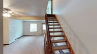 This three-floor property offers a practical and functional layout across its levels. The main living area is generously proportioned, featuring wall-to-wall carpet, neutral painted walls, and a ceiling fan with integrated lighting. A large window allows natural light to fill the room, creating a bright and open atmosphere. Structural beam detailing adds a subtle architectural element to the space.

The kitchen is outfitted with light wood cabinetry, granite-look countertops, and an exterior door that provides convenient outdoor access. The staircase connecting the floors features dark wood railings and balusters with carpeted treads, offering a classic residential look.

Bathrooms include a full bath with a tub-shower combination, a wood-toned vanity, and tile flooring, as well as a half bath accessible from the main level. Doors throughout feature a traditional six-panel design with dark wood trim.

The lower level includes an attached garage with a standard roll-up door and concrete flooring, along with a dedicated laundry area equipped with a washer and dryer, a utility sink, and additional storage space set within a painted concrete block utility room. Textured ceilings are found throughout much of the home.