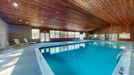 Located at 1286 Hatfield Dr in Evansville, Indiana, this single-story amenity facility is designed to provide a comprehensive recreational experience. The centerpiece of the space is a generously sized indoor swimming pool, housed beneath a striking vaulted wood-planked ceiling that lends warmth and a classic aesthetic to the environment. Recessed lighting illuminates the turquoise water, while a continuous band of large windows along the perimeter wall fills the pool hall with natural light and offers views of the surrounding greenery. The poolside deck features aggregate flooring and is furnished with lounge chairs and seating areas, creating a comfortable space for relaxation.

Adjacent to the pool area, a dedicated lounge zone features exposed brick walls, wood-paneled ceilings, and additional seating with a dining table, ideal for socializing. A sunlit corridor with floor-to-ceiling windows runs alongside the pool, providing an airy transition between spaces.

The fitness center occupies a separate wing and is carpeted throughout, offering equipment including treadmills, an elliptical machine, a multi-station weight machine, an adjustable bench, medicine balls, resistance bands, and exercise balls, making it well-suited for a variety of workout routines.