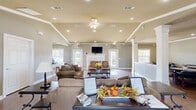 Located at 4748 Ridge Rd in North Little Rock, Arkansas, this single-story community clubhouse offers a thoughtfully designed gathering space with a warm and inviting atmosphere. The main lounge area is the heart of the facility, featuring rich hardwood flooring, vaulted ceilings with decorative crown molding, and recessed lighting complemented by a ceiling fan. A classic white-framed fireplace serves as the room's focal point, flanked by glass doors that invite natural light and provide views of the outdoors. Comfortable seating arrangements, including sofas and accent chairs, make this an ideal space for socializing and relaxation. A flat-screen television mounted above the fireplace adds a modern touch. Adjacent to the lounge is a fully equipped kitchen, appointed with rich cherry wood cabinetry, dark granite countertops, a center island with bar seating, and stainless steel appliances, including a refrigerator, dishwasher, and range. Light wood flooring and a bright window keep the kitchen feeling open and airy. A separate meeting room features hardwood floors, crown molding, and multiple round tables with leather chairs, making it well-suited for group gatherings or organized events. Throughout the space, neutral gray walls and crisp white trim create a cohesive, polished aesthetic.