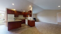 Located at 5561 Waterford Cir in Sheffield, Ohio, this single-floor residence offers a well-designed open-concept layout that seamlessly connects the kitchen and living areas. The kitchen is a standout feature, showcasing rich dark-wood cabinetry extending to the ceiling for generous storage, granite-topped counters, a central island with additional workspace, and wood-style flooring. White appliances including a range, dishwasher, and refrigerator are neatly integrated throughout. Recessed lighting illuminates the space, while a large arched window at the far end of the kitchen admits natural light and provides a view to the outdoor deck beyond.

The adjoining living area transitions to plush carpeting and benefits from vaulted ceilings that lend an airy, open feel. Multiple windows supply natural light throughout. The bedrooms are carpeted and comfortably proportioned, each featuring windows that bring in additional daylight. The bathroom is finished with rich wood vanity cabinetry, a framed mirror, and a glass-door walk-in shower with wood-style flooring, delivering a clean and functional aesthetic throughout the home.