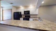This single-floor residence at 5680 Hibernia Dr in Columbus, Ohio offers a functional and comfortable layout designed for everyday living. The open-concept kitchen is a central highlight, featuring white cabinetry, stone-look laminate countertops, a peninsula breakfast bar, and a full suite of black appliances including a refrigerator, gas range with over-the-range microwave, and a stainless steel sink. Recessed lighting illuminates the space, which flows seamlessly into the living area. The living room is generously proportioned, finished with neutral-toned wall-to-wall carpeting, warm wood baseboards, and recessed lighting, creating a bright and welcoming atmosphere. A hallway connects the main living areas to the private quarters. The bedrooms are well-sized, each outfitted with plush carpeting, ceiling fans with light fixtures, and windows that invite natural light. The bathroom features a wide vanity with a white countertop, under-sink cabinetry, a large mirror, louvered medicine cabinet, and a combination tub and shower. Throughout the home, a consistent neutral color palette and textured ceilings contribute to a cohesive, move-in-ready aesthetic.