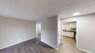 This single-floor residence presents a clean, modern aesthetic through its consistent use of neutral gray tones, white trim, and updated finishes. The open living area is anchored by durable wood-look plank flooring and features a full-width sliding glass door that floods the space with natural light while providing direct outdoor access and views of the surrounding exterior.

The kitchen is a standout feature, showcasing crisp white cabinetry paired with a classic white subway tile backsplash and dark countertops. Black appliances — including a refrigerator, gas range, microwave, and dishwasher — provide a bold contrast, while a skylight enhances brightness. Light-toned wood-look flooring completes the kitchen's functional, contemporary look.

The bedrooms are carpeted for comfort, each featuring textured ceilings and windows that bring in natural light. One bedroom includes a direct en-suite connection to a bathroom equipped with a dark granite-topped vanity, white cabinetry, and a shower-tub combination. A second bathroom mirrors this design with matching countertops and fixtures. Throughout the unit, consistent hardware finishes and neutral wall colors establish a cohesive and polished overall ambiance.