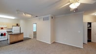 Located in Duncanville, this single-story space presents a practical and well-maintained layout designed for comfortable everyday living. The main living area is finished with plush wall-to-wall carpeting that lends a warm, cozy feel underfoot. Crown molding runs along the ceiling perimeter, adding a refined architectural detail that elevates the overall aesthetic. Overhead, a combination of track lighting and a ceiling fan provides both focused and ambient illumination while supporting air circulation throughout the room. The walls are painted in a neutral, light tone that enhances the sense of openness and pairs well with natural light filtering in from a window visible in the adjoining room. A central partition wall creates a natural division within the space, offering subtle separation between areas without completely closing them off. HVAC vents are integrated into the walls and ceiling, ensuring efficient climate control throughout. A partial view of cabinetry suggests additional functional space nearby. The overall ambiance is clean, bright, and move-in ready, making it a versatile space well-suited to a variety of uses and furnishing styles.