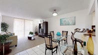 This single-floor residence offers a thoughtfully laid-out living space with a comfortable and neutral aesthetic throughout. The living room serves as the heart of the home, featuring plush wall-to-wall carpeting, a textured ceiling, and a large sliding glass door dressed with vertical blinds that flood the room with natural light. The open feel is enhanced by clean white walls, framed artwork, and a seamless transition into the tiled dining area. The kitchen is designed for practicality, featuring a U-shaped layout with ample cream cabinetry, dark countertops with a coordinating tile backsplash, recessed lighting, white tile flooring, and a full suite of appliances including a dishwasher, electric range, and range hood. The generously sized bedroom offers soft carpeting, vertical-blind windows that invite natural light, a walk-in closet with built-in shelving, and ample space for a full furniture arrangement. The bathroom is clean and functional, finished with white tile flooring, a tub-shower combination, a vanity with storage, and bright, neutral walls. Overall, the residence presents a bright, calm atmosphere with consistent finishes and a practical floor plan.