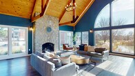 Located at 5191 Fairway Lakes Drive in Columbus, Ohio, this single-story community clubhouse is a standout example of thoughtful architectural design and modern amenities. The centerpiece of the space is a sweeping great room defined by soaring vaulted ceilings clad in warm natural wood with exposed timber beams, bold teal accent walls, and rich hardwood flooring throughout. A dramatic floor-to-ceiling stone fireplace anchors one end of the room, while a grand arched window on the opposite wall frames stunning views of an outdoor fountain and pond, flooding the interior with abundant natural light. Pendant chandeliers with Edison-style bulbs complement the warm, inviting atmosphere. The open layout seamlessly connects the lounge area to a dining space and a sleek kitchen bar with white countertops and bar-height seating, ideal for gatherings and community events. The fitness center is well-appointed with a variety of cardio and strength equipment, rubber flooring, mirrored walls, and its own arched window that brings in natural light. A dedicated leasing office features glass partition walls, wood shelving, and modern workstations. The overall ambiance balances rustic charm with contemporary sophistication, creating a welcoming and functional community hub.