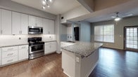 Located at 300 Seaforth Dr in Durham, NC, this single-floor residence offers a thoughtfully designed open-concept layout with modern finishes throughout. The kitchen serves as a central highlight, featuring crisp white cabinetry extending to the ceiling, a subway tile backsplash, granite countertops, and a full suite of stainless steel appliances including a gas range, over-the-range microwave, and refrigerator. A peninsula with a granite overhang provides additional counter space and a natural transition into the expansive living area, which is finished with rich dark hardwood-style flooring and crown molding. A ceiling fan and generous natural light from large windows enhance the open feel of the living space. The bedrooms are carpeted for comfort, with one featuring a ceiling fan and direct access to a walk-in closet equipped with wire shelving. A second bedroom offers a window with outdoor views. The bathroom is cleanly finished with wood-style flooring, a granite-topped vanity with white cabinetry, and a full tiled tub-shower surround. The unit's neutral gray tones and consistent modern finishes create a cohesive and functional living environment throughout.