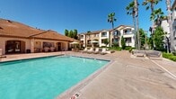Located at 801 E Atherton Dr in Manteca, California, this beautifully maintained outdoor amenity space is the centerpiece of the Paseo Villas residential community. The grounds showcase Mediterranean-inspired architecture, characterized by stucco exteriors, arched windows, terra cotta tile rooflines, and multi-story residential buildings with private balconies overlooking the courtyard.

The highlight of the space is a generously sized resort-style swimming pool with crystal-clear turquoise water, complemented by a separate spa and surrounding sundeck. Lounge chairs, patio umbrellas, and wood-slatted outdoor furniture are thoughtfully arranged throughout the pool deck, creating inviting areas for relaxation.

The landscaping throughout the property is meticulously maintained, featuring tall swaying palm trees, trimmed hedgerows, flowering plants, and lush greenery that provides both privacy and visual appeal. Dedicated walking paths wind through the grounds, connecting the various outdoor areas.

A clubhouse structure with arched facades and large windows anchors one side of the community, offering additional amenity space. Ornamental fencing, accent lighting, and carefully curated plantings add to the polished, well-kept atmosphere. Under the consistently sunny Central Valley skies, this outdoor space delivers a vibrant, resort-like experience for residents.