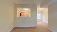 This two-floor residence offers a thoughtfully designed interior that balances functionality with comfortable living. The main level showcases an open-concept layout where the living and dining areas flow seamlessly together, unified by soft, neutral wall tones and plush wall-to-wall carpeting that adds warmth underfoot. Natural light filters in through well-placed windows, brightening the space and creating an airy, welcoming ambiance.

A standout architectural detail on the main level is the pass-through window connecting the kitchen to the living area, providing both visual openness and practical convenience. The kitchen features light wood cabinetry with ample storage, a built-in microwave, and a refrigerator, all set beneath a recessed ceiling light that illuminates the workspace effectively. The pass-through countertop also serves as a casual bar or serving area, enhancing the home's entertaining potential.

The dining area is anchored by a elegant pendant light fixture, adding a refined focal point to the space. Crown molding details along the ceilings contribute a classic, polished finish throughout. Spanning two floors, the home offers distinct zones for living and private spaces, making it well-suited for a variety of lifestyle needs.