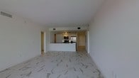 This single-floor residence showcases a clean, contemporary design with an emphasis on open living. The space is anchored by striking marble-style porcelain tile flooring that runs throughout, lending a refined and upscale aesthetic to the interior.

The open-concept layout seamlessly connects the living area to the kitchen, creating a spacious and airy environment. The kitchen is well-appointed with white cabinetry, a peninsula with bar-height countertops, and a full suite of stainless steel appliances, including a refrigerator, microwave, and range. Track lighting above the kitchen workspace ensures excellent task illumination, while the overall white-toned palette keeps the space feeling bright and cohesive.

The smooth white ceilings and neutral walls contribute to a minimalist atmosphere that is both functional and visually appealing. Doorways visible from the main living area suggest additional rooms beyond, providing a sense of depth and privacy within the layout. Ventilation is handled discreetly through flush ceiling registers that maintain the clean lines of the design.

Overall, this residence offers a polished, modern living environment with thoughtful finishes and an efficient, well-connected floor plan suited to contemporary living.