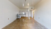 Located at 1 N Fifth Ave in downtown Tucson, Arizona, this one-bedroom, one-bathroom unit offers an urban, industrial aesthetic defined by white-painted concrete block walls and polished concrete floors throughout. The open living area flows directly into a functional kitchen equipped with a range, refrigerator, and open wire shelving, all set against tiled walls. A sliding glass door leads from the living space to a private balcony, allowing natural light to fill the interior and providing views of the surrounding cityscape.

The generously sized bedroom features the same concrete block construction, a full-panel closet for storage, and direct access to the hallway. The bathroom includes a full-size soaking tub and shower combo with beige tile surround, a toilet, and grab bar fixtures. A dedicated hallway connects the main living areas and provides access to both the bedroom and bathroom.

Throughout the unit, the consistent use of white-painted masonry walls and raw concrete flooring lends a clean, utilitarian character. Ceiling-mounted light fixtures and HVAC vents are integrated into the layout. The unit's compact and efficient single-floor plan makes practical use of its footprint, offering a straightforward layout well-suited to urban living in the heart of Tucson.