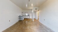 Located at 1 N Fifth Ave in downtown Tucson, Arizona, this one-bedroom, one-bathroom unit offers an urban, industrial aesthetic defined by white-painted concrete block walls and polished concrete floors throughout. The open living area flows directly into a functional kitchen equipped with a range, refrigerator, and open wire shelving, all set against tiled walls. A sliding glass door leads from the living space to a private balcony, allowing natural light to fill the interior and providing views of the surrounding cityscape.

The generously sized bedroom features the same concrete block construction, a full-panel closet for storage, and direct access to the hallway. The bathroom includes a full-size soaking tub and shower combo with beige tile surround, a toilet, and grab bar fixtures. A dedicated hallway connects the main living areas and provides access to both the bedroom and bathroom.

Throughout the unit, the consistent use of white-painted masonry walls and raw concrete flooring lends a clean, utilitarian character. Ceiling-mounted light fixtures and HVAC vents are integrated into the layout. The unit's compact and efficient single-floor plan makes practical use of its footprint, offering a straightforward layout well-suited to urban living in the heart of Tucson.