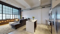 This single-floor urban loft masterfully blends industrial character with modern refinement. The open-plan living and kitchen area serves as the heart of the space, anchored by dramatic floor-to-ceiling factory-style windows framed in dark metal, set against exposed dark brick — a striking architectural feature that draws in abundant natural light. Soaring ceilings with exposed structural beams and visible HVAC ductwork reinforce the loft's industrial aesthetic, while polished concrete floors run throughout, lending a cohesive, contemporary feel.

The kitchen is well-appointed with warm wood-grain lower cabinetry, clean white upper cabinetry and open shelving, a subway tile backsplash, stainless steel appliances, and a sleek white island with bar seating — ideal for both cooking and casual dining.

A long hallway with wall sconces connects the living area to the private rooms. The bedroom is a calm, minimal retreat with soft neutral tones, track lighting, a large sliding-panel closet, and wood flooring. An in-unit laundry room with a full-size washer and dryer adds everyday convenience. The overall ambiance is sophisticated yet comfortable, balancing raw industrial elements with clean, modern finishes throughout.