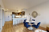 Located at 120th Ave NE in Bellevue, WA, this one-bedroom, one-bathroom residence offers a well-designed, open-concept layout with consistent hardwood-style flooring throughout. The combined kitchen and living area serves as the heart of the home, featuring a peninsula with bar seating, rich dark wood cabinetry, white quartz countertops, a subway tile backsplash, and a full suite of stainless steel appliances including a refrigerator, range, microwave, and dishwasher. Pendant lighting above the peninsula adds a modern touch. The adjacent dining area provides ample space for a full dining set, while the living room is anchored by floor-to-ceiling windows that flood the space with natural light and offer open views of the surrounding Bellevue skyline and greenery. The bedroom features its own large window, creating a bright and airy atmosphere, and connects directly to a dedicated closet with built-in shelving and hanging rods. The bathroom is finished with clean white subway tile surrounding a full soaking tub and shower combination, complemented by a wood-toned vanity and light flooring. Throughout the residence, a neutral color palette and contemporary finishes create a cohesive, modern ambiance.