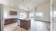 Located in Rathdrum, Idaho, this one-bedroom, one-bathroom unit offers a well-designed layout across a single floor. The open-concept living, dining, and kitchen area is immediately impressive, anchored by soaring vaulted ceilings that lend a sense of spaciousness well beyond the unit's footprint. Light hardwood-style flooring runs throughout the main living areas, complementing the neutral color palette and crisp white walls.

The kitchen is a standout feature, equipped with rich dark-toned cabinetry, light quartz countertops, a central island with an undermount sink and dishwasher, and a full suite of stainless steel appliances including a range, microwave, and refrigerator. Stylish gold pendant lights hang above the island, adding a warm, modern accent. Large windows and a sliding glass door open to a private balcony, framing scenic mountain views and filling the space with natural light.

The bedroom is generously sized with plush carpet flooring, vaulted ceilings, and a window offering additional views of the surrounding area. The full bathroom features a tub-shower combination, a dark-cabinet vanity with quartz countertop, light tile-style flooring, and textured walls for added character. This unit combines modern finishes with an airy, open feel throughout.