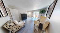 Located at 4501 Shepard St NE in Albuquerque, New Mexico, this efficiently designed single-floor unit offers a cohesive and thoughtfully arranged living space. The open-concept living area is finished with light-toned luxury vinyl plank flooring that runs throughout, lending a clean and modern aesthetic. A textured ceiling adds architectural character, while neutral gray walls provide a versatile backdrop. Large sliding glass doors flood the living area with natural light and open directly onto a private outdoor patio, creating a seamless indoor-outdoor connection. A wall-mounted air conditioning unit ensures year-round comfort. The compact kitchen is positioned adjacent to the main living space and features white cabinetry, black appliances including a stove and refrigerator, and a skylight overhead that brings in additional natural light. The entrance leads through a hallway that connects the living area to the bathroom. The bathroom is neatly appointed with a white vanity, mirror, and stylish decorative accents including gold sunburst wall art and pendant lighting, giving it a polished, boutique feel. Overall, the unit presents a bright, organized, and cohesive living environment well-suited for comfortable everyday living.