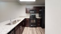 This two-floor residence is designed with a clean, modern aesthetic and a practical layout that makes efficient use of space throughout both levels. The main floor features wood-style plank flooring that extends through the living area and into the kitchen, creating a cohesive and easy-to-maintain foundation. A staircase connects the two floors, positioned alongside a hallway that leads to additional rooms and storage. The kitchen is well-equipped with rich dark cabinetry, granite-style countertops, a full suite of black appliances including a refrigerator, range, and built-in microwave, and a stainless steel sink. A peninsula counter separates the kitchen from the adjacent living space, adding both function and definition to the open layout. A half bathroom on the main level includes a dark-cabineted vanity with a granite countertop and wood-style flooring. Upstairs, carpeted bedrooms provide a comfortable, quieter retreat, with windows allowing in natural light. A walk-in closet with dual hanging rods offers generous storage. The full upper bathroom features a tub-shower combination, a dark vanity with granite countertop, and tile flooring. A dedicated laundry area with washer and dryer hookups rounds out the upper level.