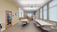 Located at 9393 Tidwell Rd in Houston, TX, this single-floor community facility is thoughtfully designed to serve a variety of educational and social functions. The space features an open, airy layout with warm yellow accent walls, neutral gray tones, and durable flooring throughout, creating a welcoming and functional environment.

The main activity area is generously proportioned, accommodating multiple white rectangular tables and modern stackable chairs arranged to support group gatherings, workshops, or collaborative sessions. Overhead linear lighting and ceiling fans ensure the area remains well-lit and comfortable. Large windows fitted with roller shades allow ample natural light to fill the room.

A dedicated kitchen area lines one wall and is equipped with stainless steel appliances including a full-size refrigerator, dishwasher, and microwave, complemented by light maple cabinetry and a continuous countertop with a sink — making it well-suited for community meals or events.

A children's corner provides a nurturing, age-appropriate space outfitted with small wooden tables and chairs, a bookshelf stocked with learning materials, and playful wall décor. A cozy seating area with a compact sofa offers a comfortable spot for reading or supervision.

A computer workstation area with desktop computers and ergonomic seating supports digital learning and productivity. Together, these distinct zones make this facility a comprehensive, community-centered resource.